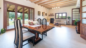 A spacious living area with a dining table, chairs, and a sofa. There are large windows and a view of the outdoors.