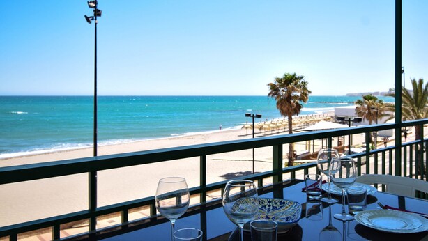 A table with empty wine glasses and plates, overlooking a beach with palm trees and a clear blue sky. - Ref: 237 Beachfront apartment in Carvajal with amazing sea views (Fuengirola)