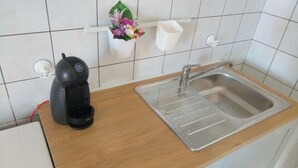 Una cucina con una macchina da caffè, un lavandino e uno scaffale con un vaso di fiori.