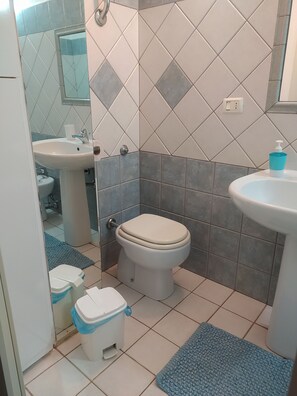 A bathroom with a toilet, sink, and mirror. There are blue mats on the floor.