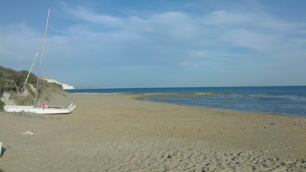 Una spiaggia sabbiosa con una barca a sinistra e un mare calmo.