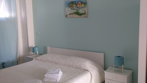Un letto rifatto con asciugamani piegati, un comodino con una lampada e un quadro appeso al muro.