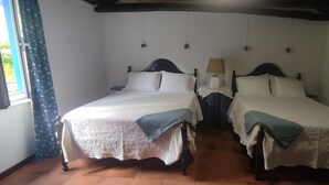 Habitación con dos camas, cada una con cabecero de madera, una mesita de noche con lámpara y ventana con cortinas.
