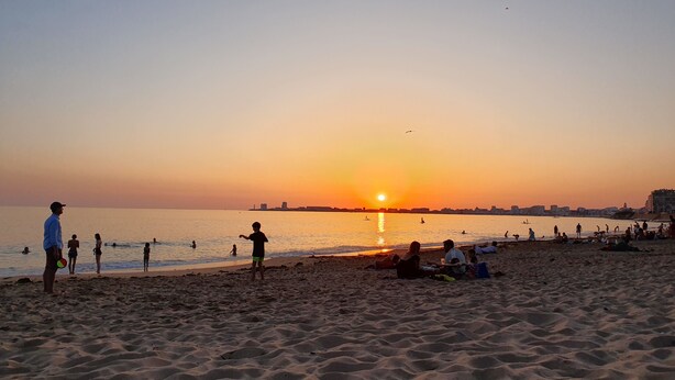 A beach with people relaxing and playing, a sunset in the background, and a city skyline across the water. - Charming Vendée house with small enclosed garden (Olonne-sur-Mer)