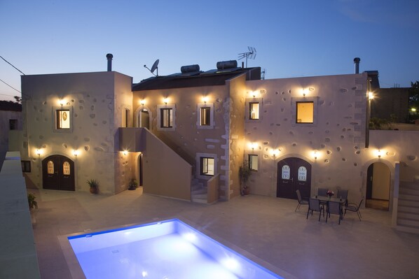 A building with multiple windows and doors, a swimming pool, and outdoor seating.