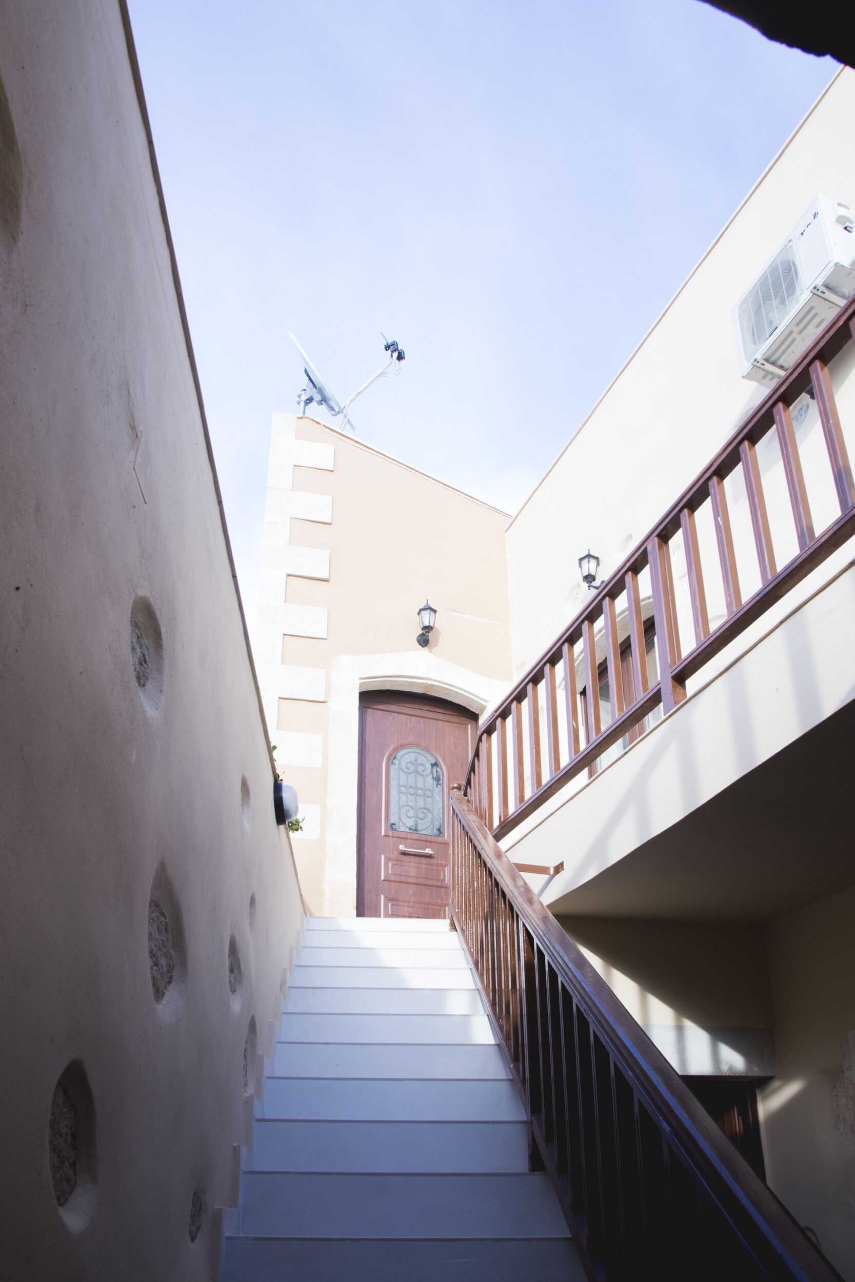 Un escalier étroit avec une rampe en bois menant à une porte dotée d’une fenêtre.