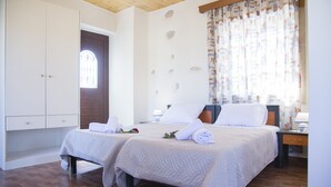 Una habitación de hotel con dos camas, un armario, una ventana con cortinas y suelo de madera.