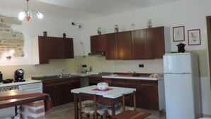 A compact kitchen with wooden cabinets, a dining table with chairs, a refrigerator, and a chandelier. - Isolated on hill, flat with private terrace among romanesque art,quiet,nature. (Cocconato)