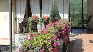 A balcony with a tiled roof, white curtains, and a view of greenery. - Isolated on hill, flat with private terrace among romanesque art,quiet,nature. (Cocconato)