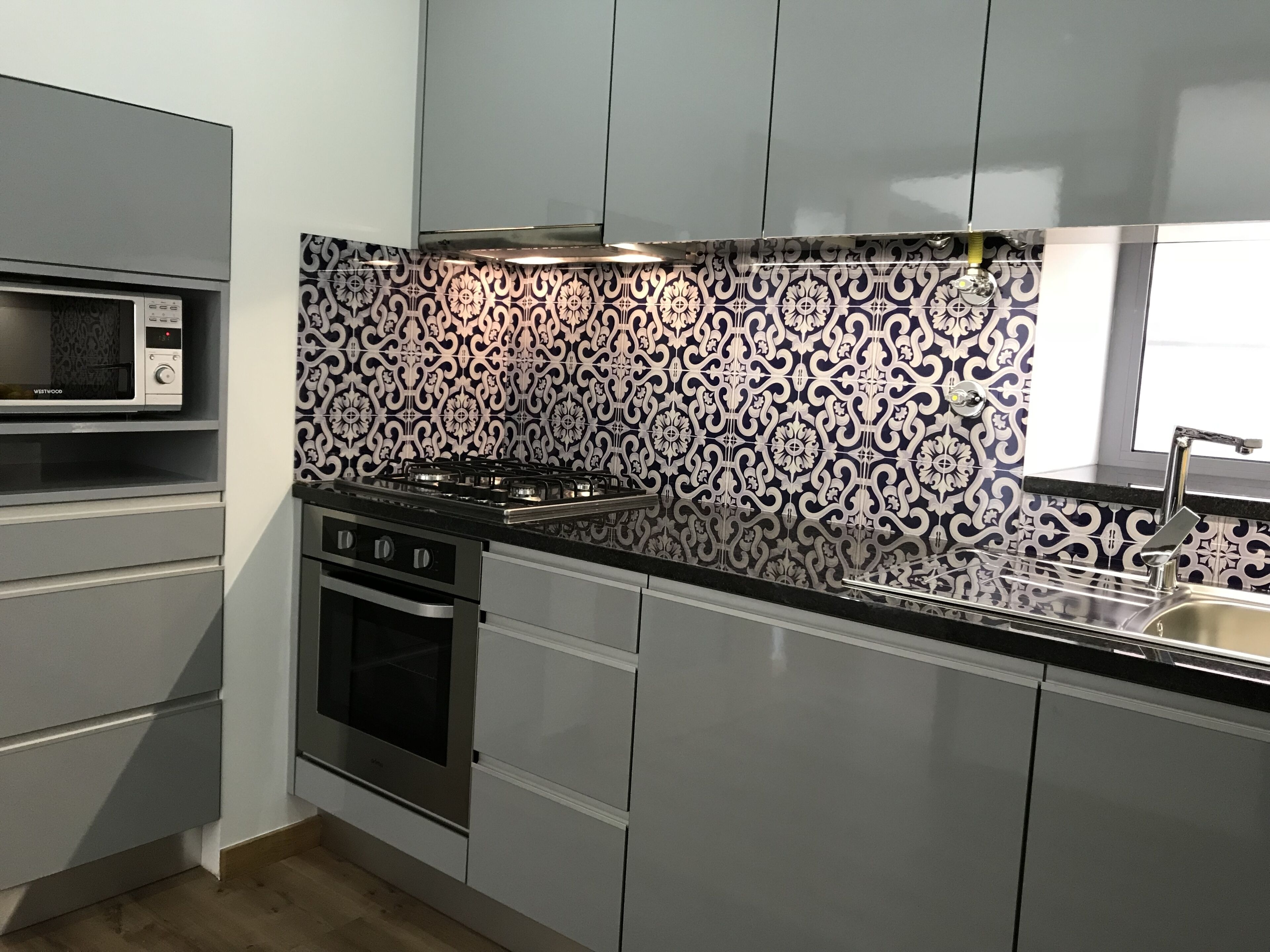 Een moderne keuken met grijze kastjes, een zwart aanrecht, een magnetron, een fornuis en een spoelbak.