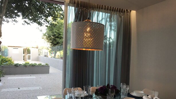 A dining table set for four with a glass top, surrounded by white chairs, and a hanging light fixture above.