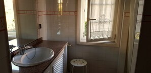 Een badkamer met een wastafel, spiegel en raam.