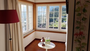 Ein Zimmer mit einem großen Fenster, einem Tisch mit einer Laterne und Blumen, sowie einer roten Lampe.