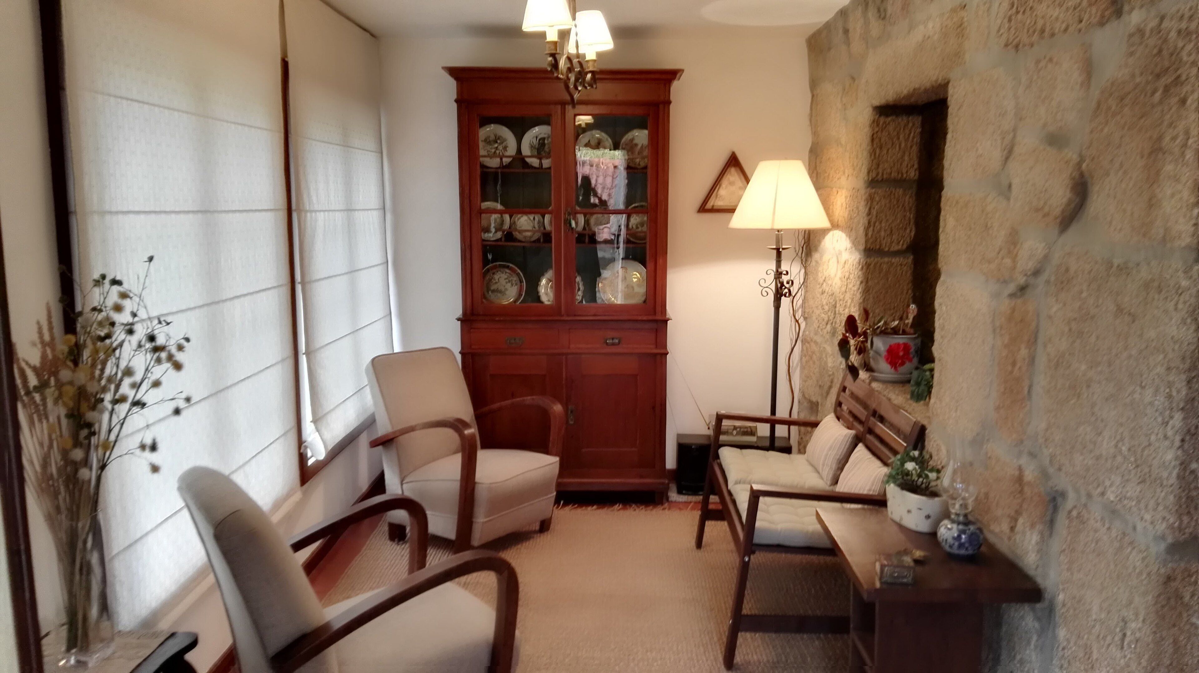 A cozy room with a fireplace, two armchairs, a wooden cabinet with glass doors, and a floor lamp.
