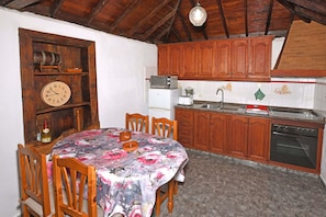 Una cocina con armarios de madera, microondas, pileta y una mesa de comedor con sillas.