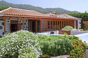 A traditional building with a tiled roof, large windows, and a garden with white and red flowers.