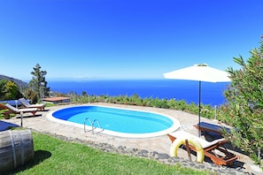 Una piscina con vista al mar, rodeada de sillas de descanso y una sombrilla.