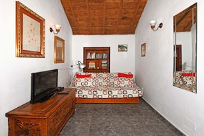 Una habitación con techo de madera, un sofá con funda estampada, una estantería y un televisor sobre un mueble de madera.