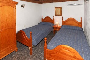 Una habitación con dos camas de madera, un armario, una mesita de noche con lámpara y aire acondicionado instalado en la pared.