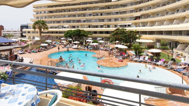 A hotel with a large pool area, multiple balconies, and outdoor seating.