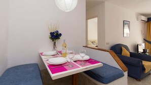 A dining area with a table set for two, a bottle of wine, and a vase with flowers.