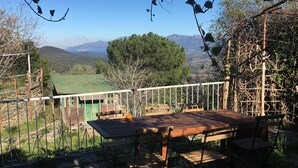 A wooden table and chairs on a balcony overlooking a green landscape with mountains in the distance. - Village house in the heart of Sorio (Sorio)