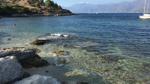 A coastal scene with clear water, rocky shore, and a sailboat in the distance. - Village house in the heart of Sorio (Sorio)