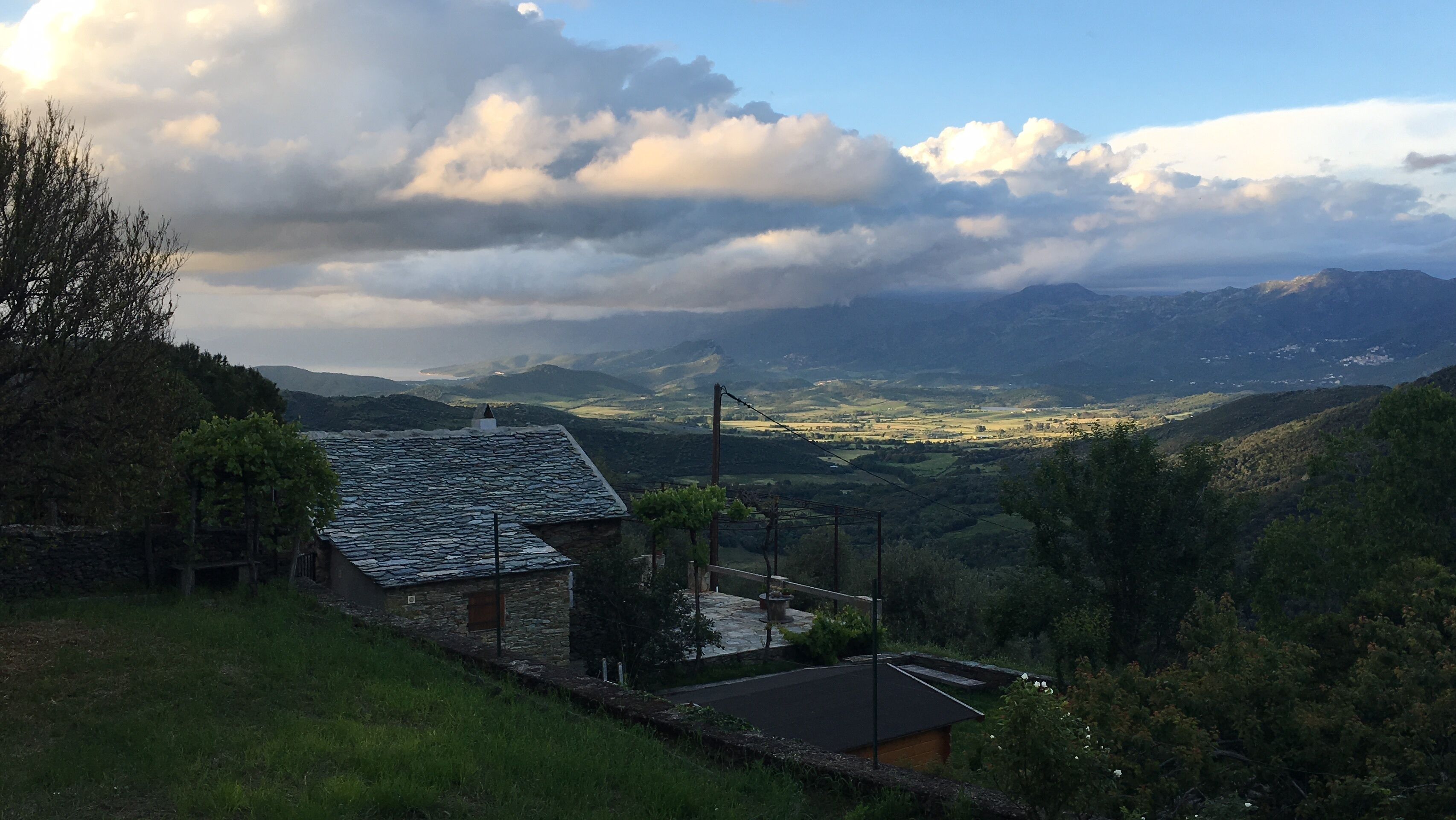 Ein rustikales Haus mit geneigtem Dach, umgeben von üppiger Vegetation und Blick ins Tal.