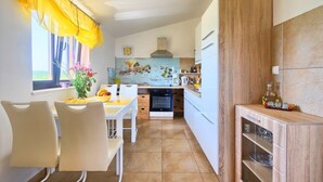 Cocina compacta con armarios blancos, horno empotrado y mueble de madera con puertas de vidrio.