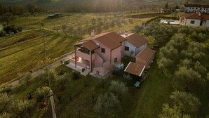 Una casa de dos pisos con techo de tejas rojas, rodeada de césped y árboles.