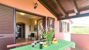 Un patio al aire libre con una mesa lista para comer, una botella de vino y un cuenco de fruta.
