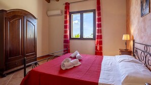 Een slaapkamer met een houten garderobe, een bed met een rode sprei, een raam met rode gordijnen en een luchtverkoeler aan de muur.