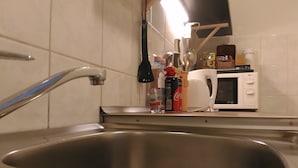 Une cuisine équipée d’un évier en acier inoxydable, d’un four à micro-ondes et de divers ustensiles de cuisine disposés sur le plan de travail.