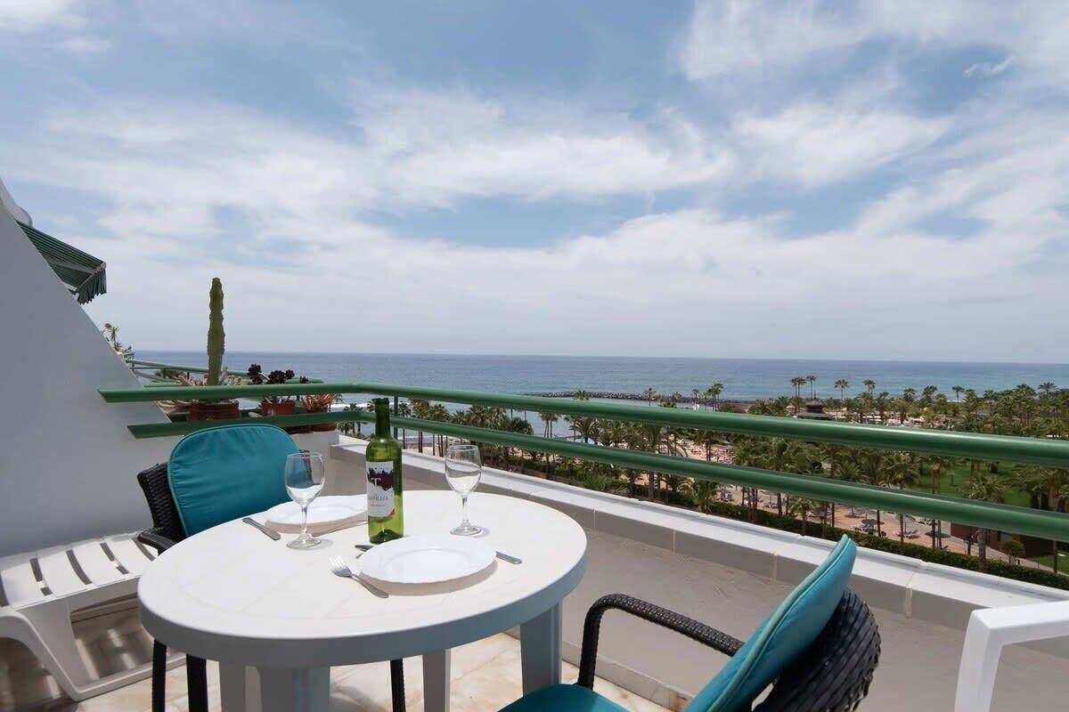Une table ronde avec une bouteille de vin, un verre et une assiette, sur un balcon donnant sur la mer.