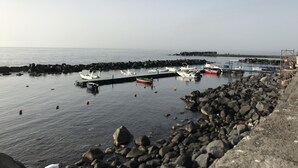 Ein Hafen mit vertäuten Booten, einer felsigen Küste und blauem Himmel.
