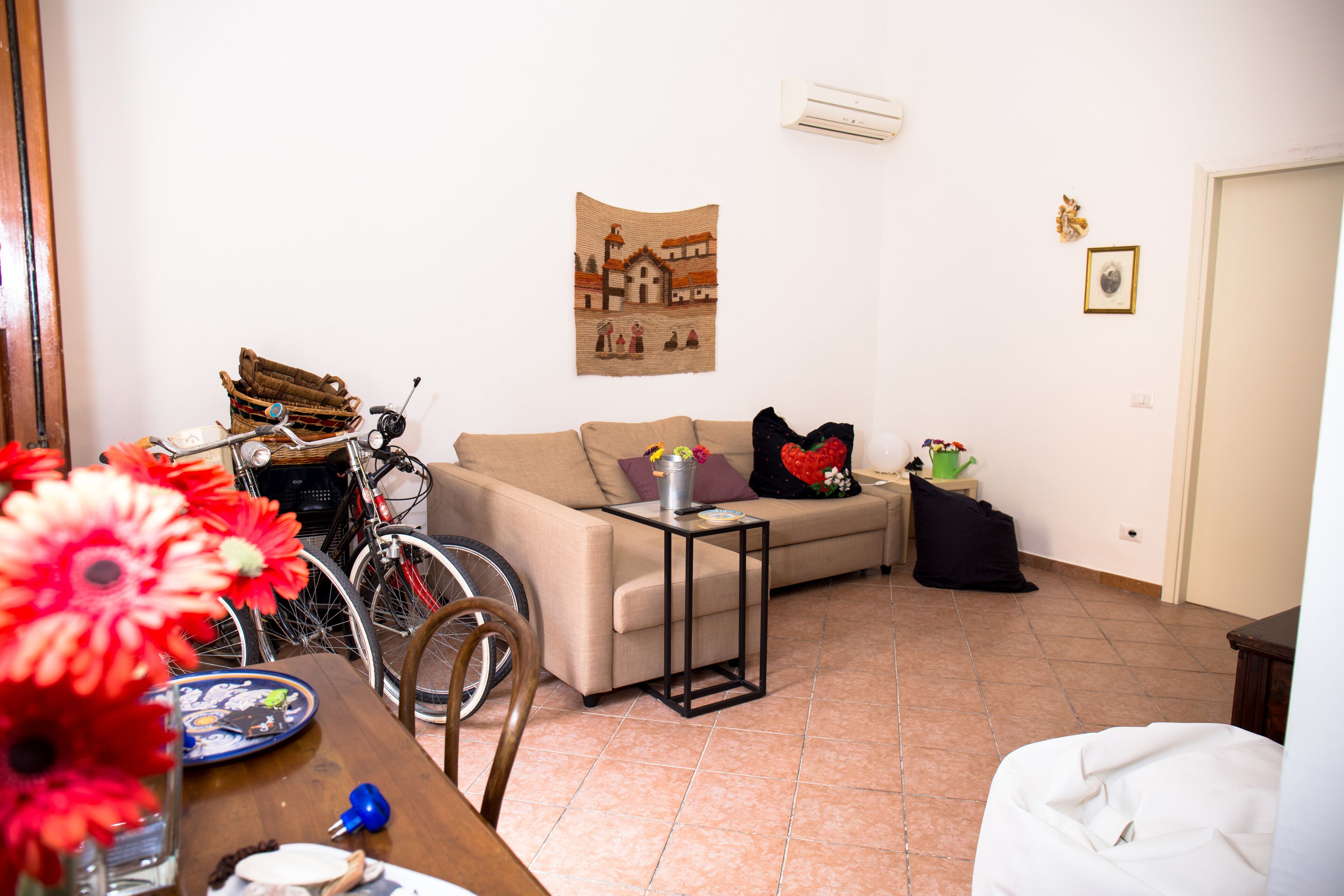 Una sala de estar con sofá, una mesa de centro, una bicicleta y un aire acondicionado instalado en la pared.