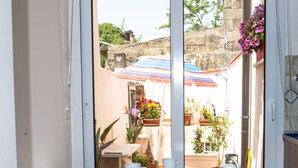 Ein kleiner Essbereich mit einem Tisch und zwei Stühlen, eine Glastür, die auf eine Terrasse mit Topfpflanzen und einem Streifen-Sonnenschirm führt.
