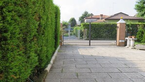 Un sendero pavimentado que conduce a una entrada con puerta de rejas, con un seto cuidado al lado.