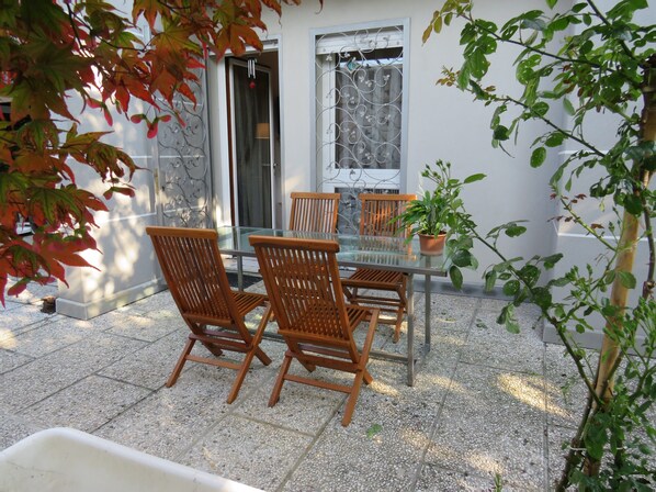 A patio with a glass table and wooden chairs, a potted plant, and a window with decorative metalwork. - Casa Giulia independent apartment (Mira)