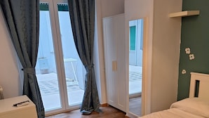 A bedroom with a bed, a bedside table, a lamp, and a view of the outside through a glass door. - NASONI DI ROMA COLOSSEUM APPARTAMENT  (until 33 people) (Roma)