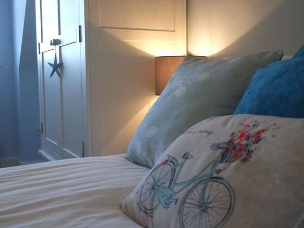 A bed with a bicycle design pillow, a blue pillow, and a lamp in the background.