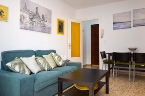 A living room with a teal sofa, a coffee table, and a dining area with chairs.