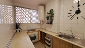 Eine kompakte Küche mit weißen Fliesen, einem eingebauten Ofen, einer Spüle und einer Uhr an der Wand.