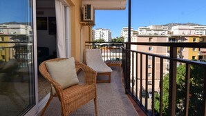 Ein Balkon mit Korbmöbeln, einer Schiebetür und Blick auf umliegende Gebäude.