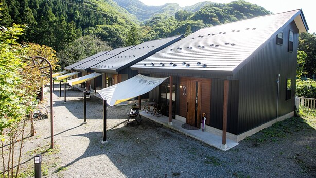 A modern building with a sloped roof, a covered outdoor seating area, and a gravel ground. - RiverStone MinakamiCampsite (Minakami)
