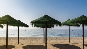 A beach with three thatched umbrellas and a clear view of the sea.