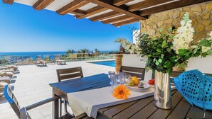 A terrace with a table set for dining, overlooking a pool and the sea.