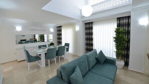 A modern living room with a teal sofa, a dining area with a glass table, and a kitchen in the background. - luxury villa for rent city D (fethiye)