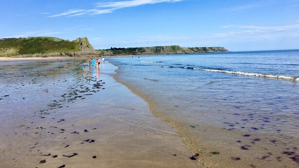 A beach with clear skies, calm water, and a distant rocky coastline. - Gower, Oxwich, Amazing Views, Sleeps 4 (Oxwich)