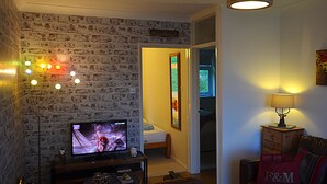 A living room with a brick wall, a television, a sofa, and a lamp. - Gower, Oxwich, Amazing Views, Sleeps 4 (Oxwich)